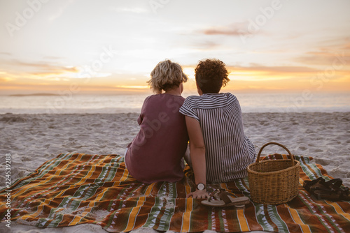 Young lesbian couple watching a romantic sunset at the beach