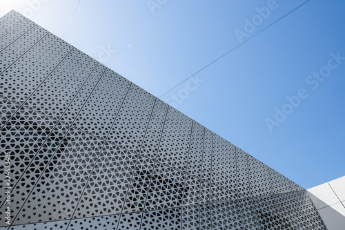 Building with white aluminum facade and aluminum panels against blue sky.