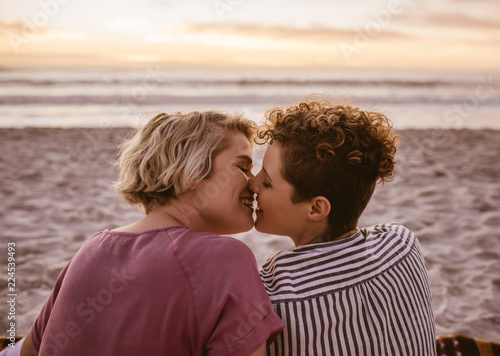 Romantic young lesbian couple kissing during a beach sunset