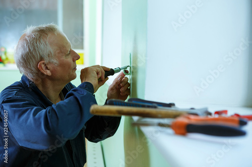 middle-aged senior man worker is working indoors fixing fitting screwing repairing