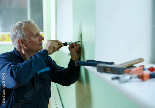 middle-aged senior man worker is working indoors fixing fitting screwing repairing