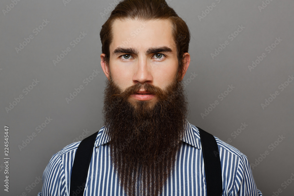 Fototapeta premium Young man in a blue shirt is standing in the studio with a serious face.Businessman is looking into the camera lens on a gray background