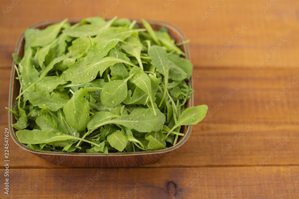 Fresh arugula salad in a bowl, on a wooden background. Fresh arugula salad in a bowl, on a wooden background.