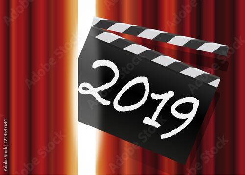 Un clap de cinéma passe au travers du rideau rouge d’une scène de spectacle avec l’inscription 2019