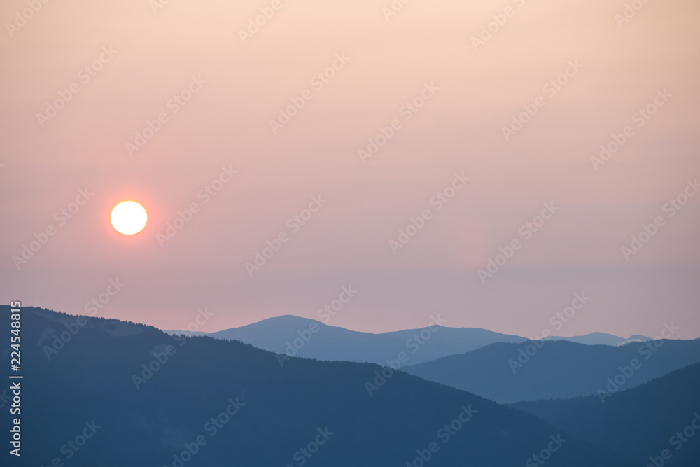 Fototapeta premium early morning in a mountain, pale sun above a mountain silhouette