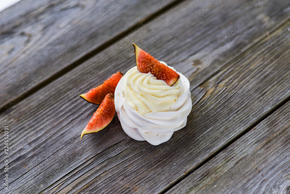 Pavlova meringue cake with figs, blueberries and mint leaves on a wooden background.