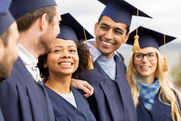 education, graduation and people concept - group of happy international students in mortar boards and bachelor gowns outdoors