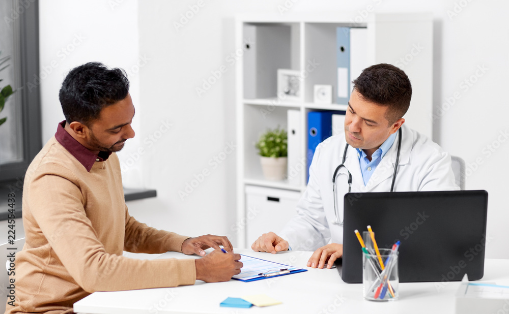medicine, healthcare and technology concept - doctor with laptop computer and male patient signing medical papers at hospital medicine, healthcare and technology concept - doctor with laptop computer and male patient signing medical papers at hospital