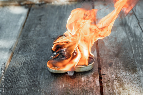 Creative background, burning shoes on a wooden background. The concept of sweat feet, bad smell, spoiled shoes after long use.