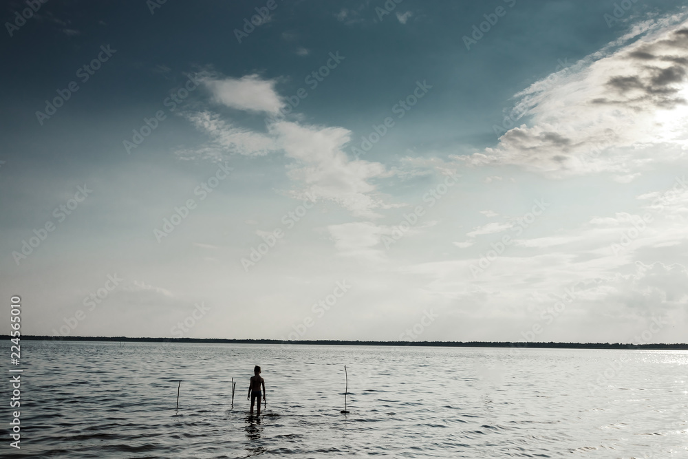 A boy standing in the lake in the morning. The child gets into the water in the dark. Creative background, mysticism, the concept of loneliness, forgetfulness.
