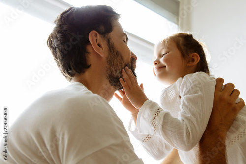 Parenthood. Family. Love. Dad is holding his little daughter in his arms and making faces. Girl is touching dad's beard and smiling. Low-angle view