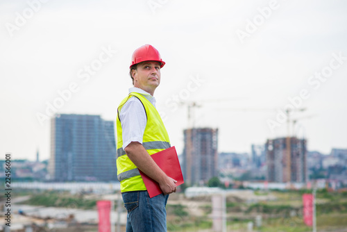 Engineer on a construction site wearing protective work wear with buildings and cranes in the background