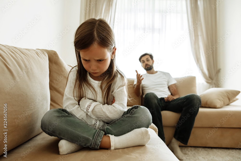 Childhood. Education. Problem. Offended little girl is crying, her father is talking to her in the background Childhood. Education. Problem. Offended little girl is crying, her father is talking to her in the background