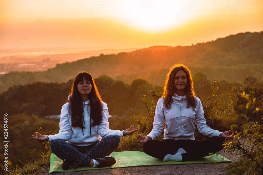 couple of women sitting at the edge of the hill. do yoga exercises on sunrise