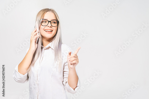 Portrait of a smiling casual very beautiful woman holding smartphone over white background and pointing finger away.