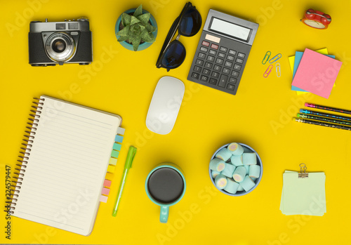 Yellow office desk table with camera, notebook, calculator, cup of coffee and supplies