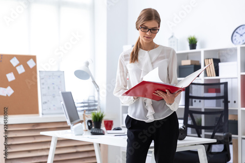Tableau sur toile A young girl stands near a computer desk and scrolls through a folder with documents