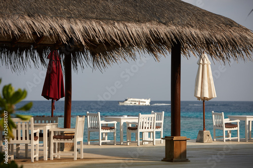 White empty table table and chairs at tropical resrraunt on open terrace in maldives. Blue ocean lagoon on background. No people.