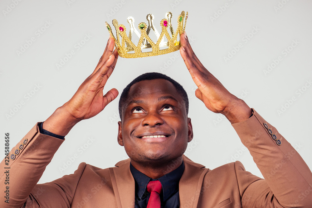 smart african american successful and rich businessman in a stylish suit and the golden crown on his head on white background in studio shot. the concept of well-deserved respect and luck