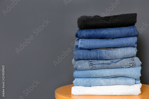 Stack of different jeans on table against gray background. Space for text