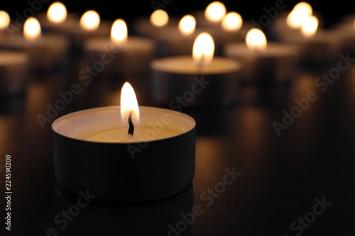 Burning candle on table in darkness  closeup with space for text. Funeral symbol