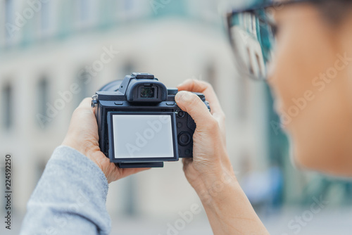 Close up of young pretty woman holding camera with blank screen. Back view.