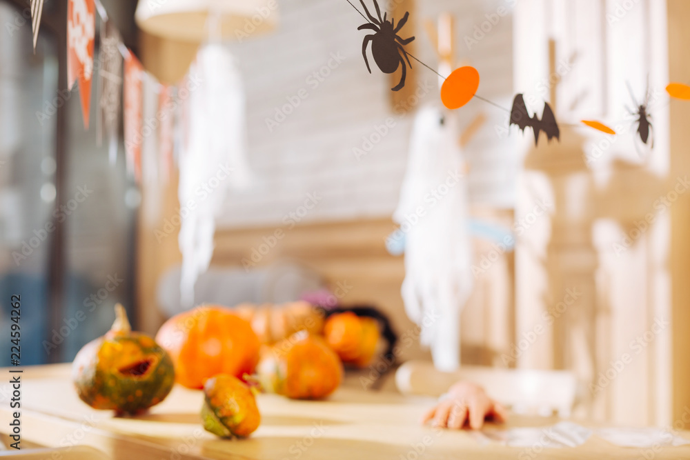Fototapeta premium Ready for Halloween. Table with paper decorations and bright pumpkins lying on it ready for Halloween children party