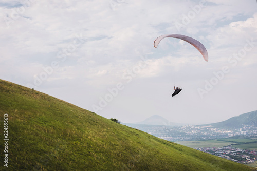 A white-orange paraglider flies over the mountainous terrain