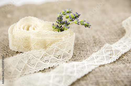 Arts and crafts background concept. Bunch on cut fresh lavender branches sticking out of a cotton lace roll, burlap cloth on background.