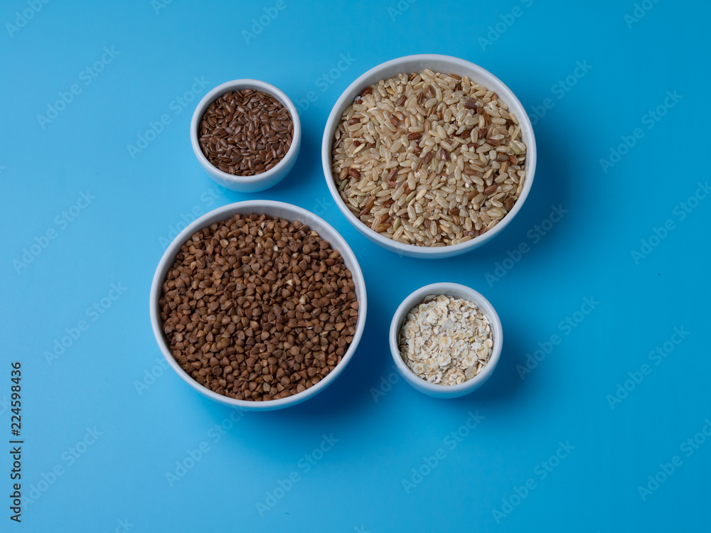 brown rice, buckwheat, flax and oat flakes in white cups on a blue background brown rice, buckwheat, flax and oat flakes in white cups on a blue background