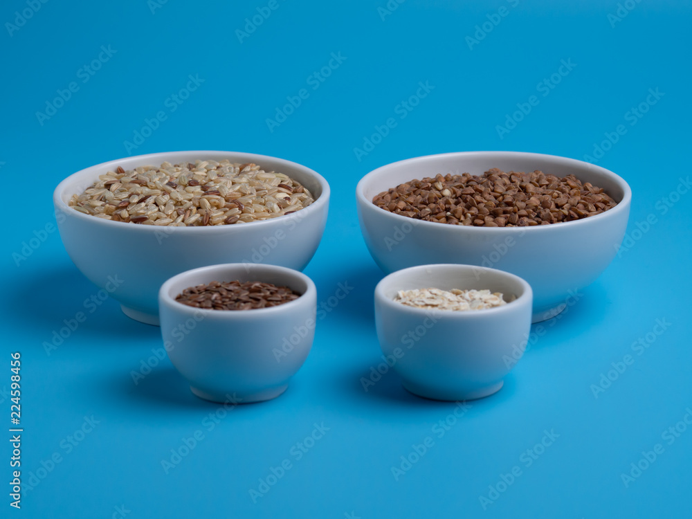 brown rice, buckwheat, flax and oat flakes in white cups on a blue background brown rice, buckwheat, flax and oat flakes in white cups on a blue background