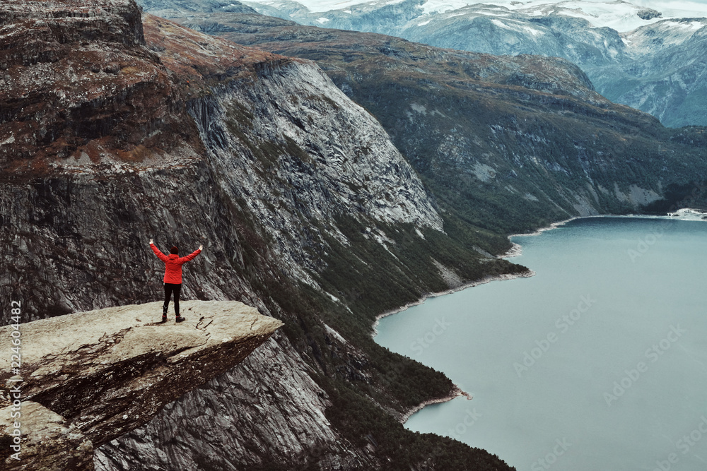 Tourist woman standing in the Trolltunga and enjoys the beautiful view of the Norwegian fjord.