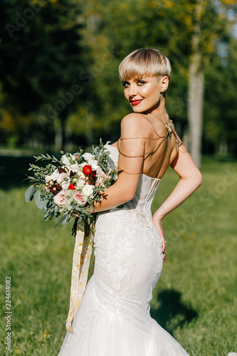 fashionable bride with short hair with a big bouquet posing in the park