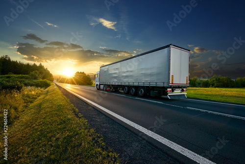 Truck driving on the asphalt road in rural landscape at sunset
