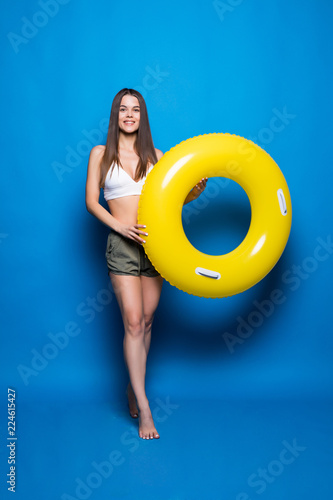 Young woman in summer wear with inflatable ring isolated over blue background