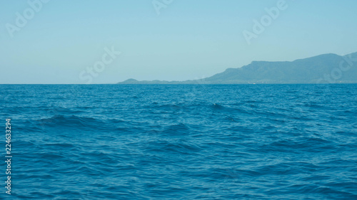 a deep blue sea with island in distance with medium water wave ripple