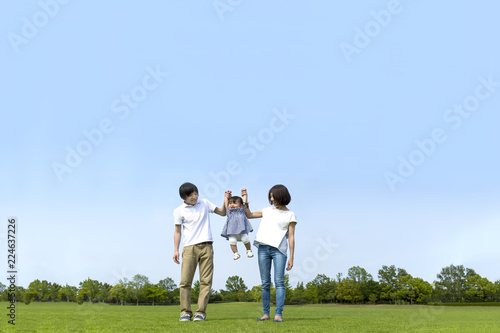 青空をバックに芝生の公園で幼い女の子と手を繋ぐ若い夫婦。幸せ、家族、親子、愛、絆イメージ