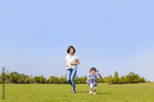 青空の下で芝生の公園で幼い女の子と走るお母さん。幸せ、子育て、愛情、遊び、健康イメージ