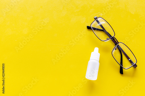 Eye health. Glasses with transparent optical lenses and eye drops on yellow background top view space for text closeup photo