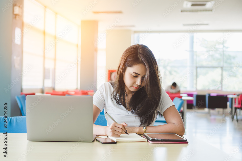 Young asian female student studying ebook online course and writing notes in library. Young asian female student studying ebook online course and writing notes in library.