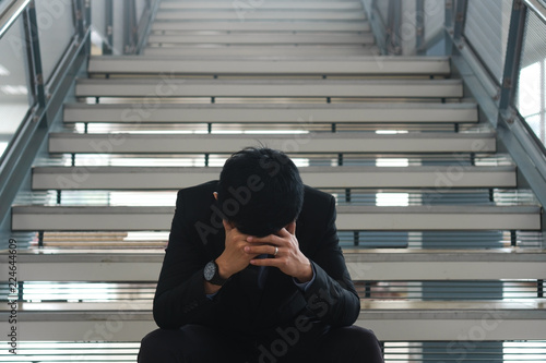 Young businessman sitting on stairs are stressing when he know business is failing and unemployed.