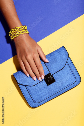Female hand with bracelets and handbag on colorful background