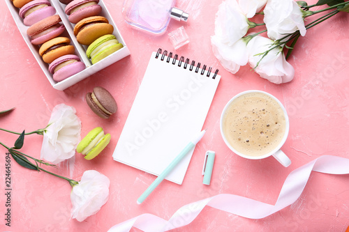 Notebook with eustoma flowers and sweet macarons on pink background