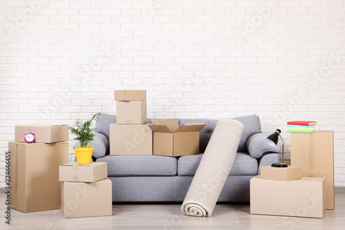 Cardboard boxes with household stuff and grey sofa on brick wall background