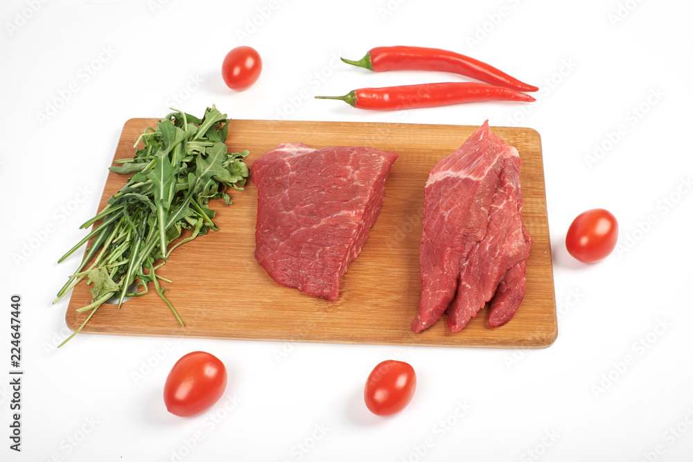 Sliced raw beef on cutting board and vegetables isolated on white background
