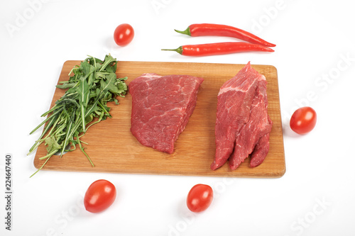 Sliced raw beef on cutting board and vegetables isolated on white background