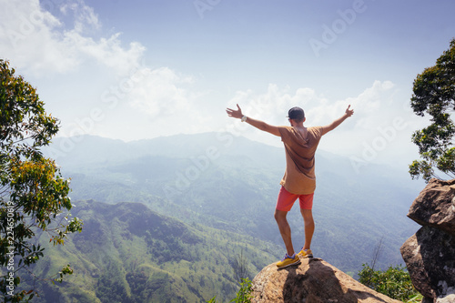Hiker standing on a peak of mountain with raised hands.