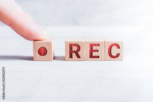 The Abbreviation REC Formed By Wooden Blocks And Arranged By A Male Finger On A White Table photo