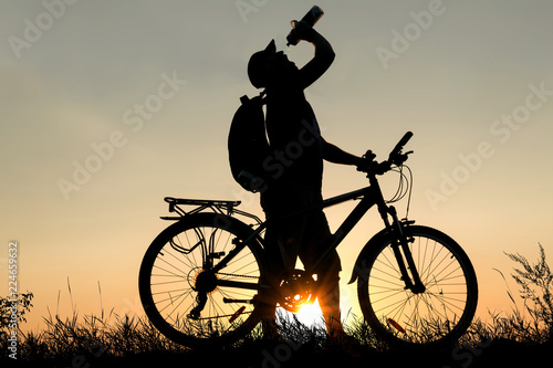 Silhouette of a man drinking water with bicycle at sunset