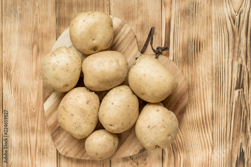 Raw potato tubers on a wooden background.